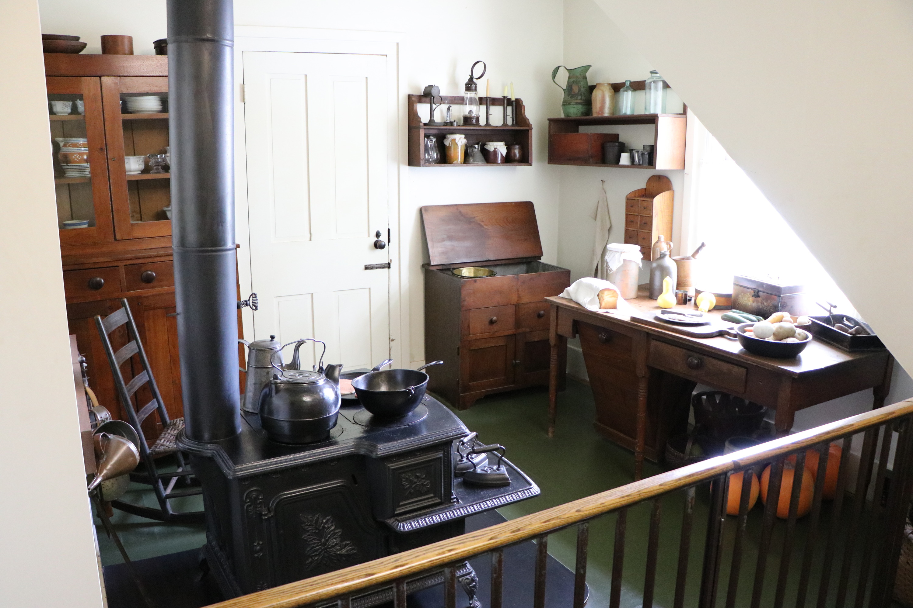 A small kitchen with a green floor, plain walls, wooden furniture, and a large cast iron stove.