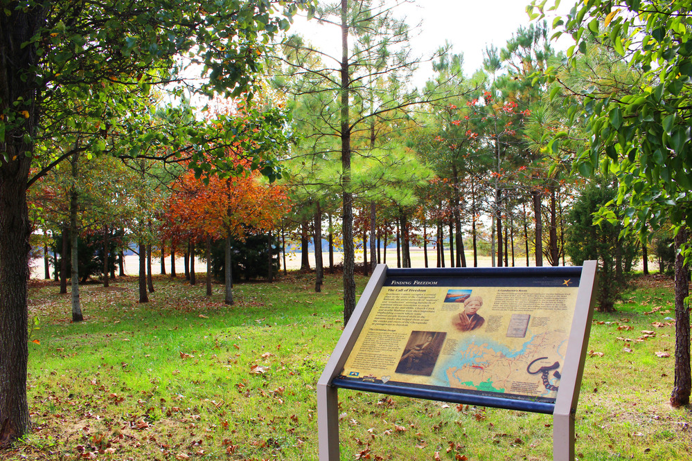 A wayside sign in a small, open grove of trees with changing fall leaves.