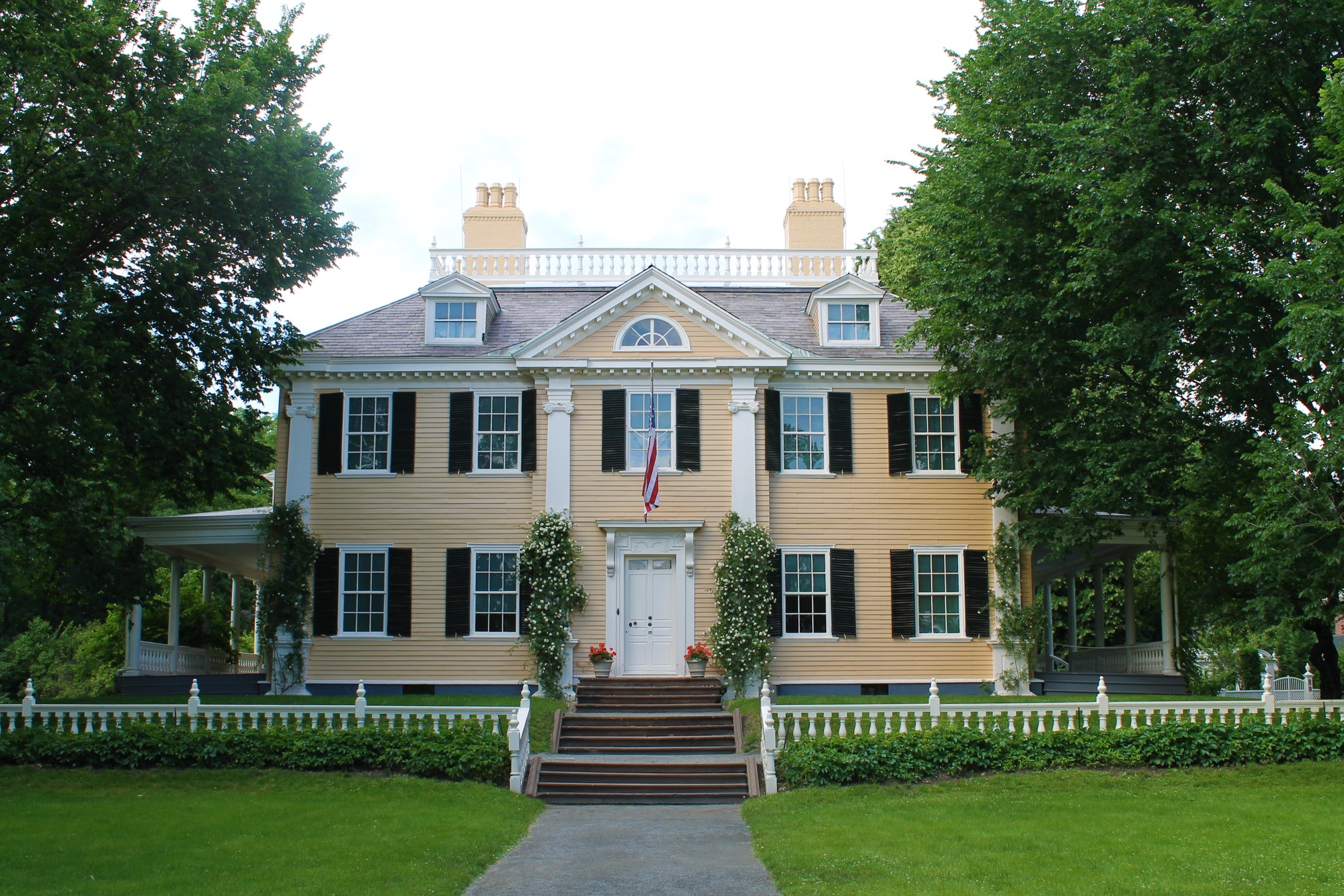 facade of yellow Georgian mansion with flag flying and green lawn and trees