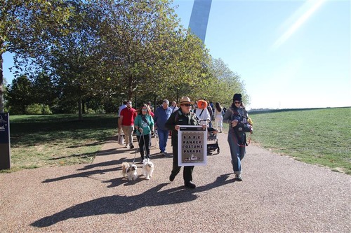 A ranger holds a sign as several humans and dogs walk behind her