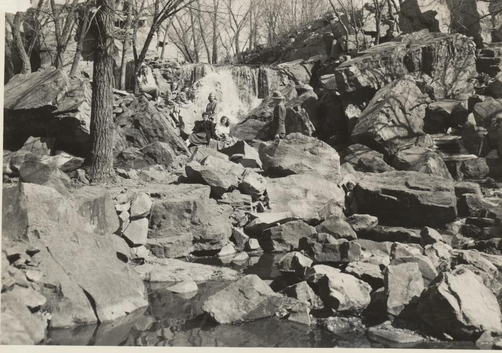 3 women seated on a boulder in a creek next to a park ranger.