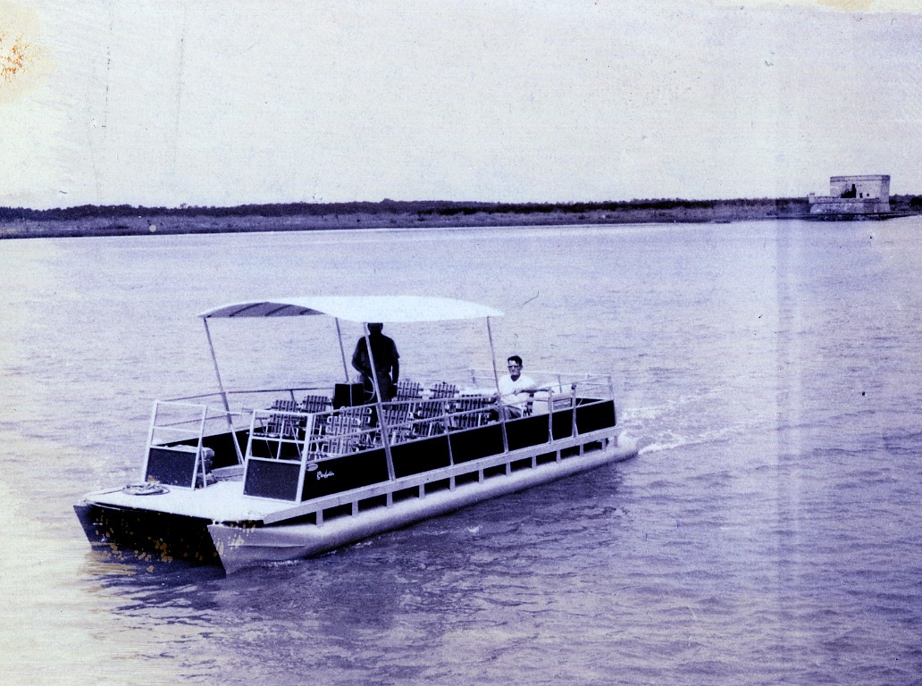 Pontoon boat with two people.  Fort in background