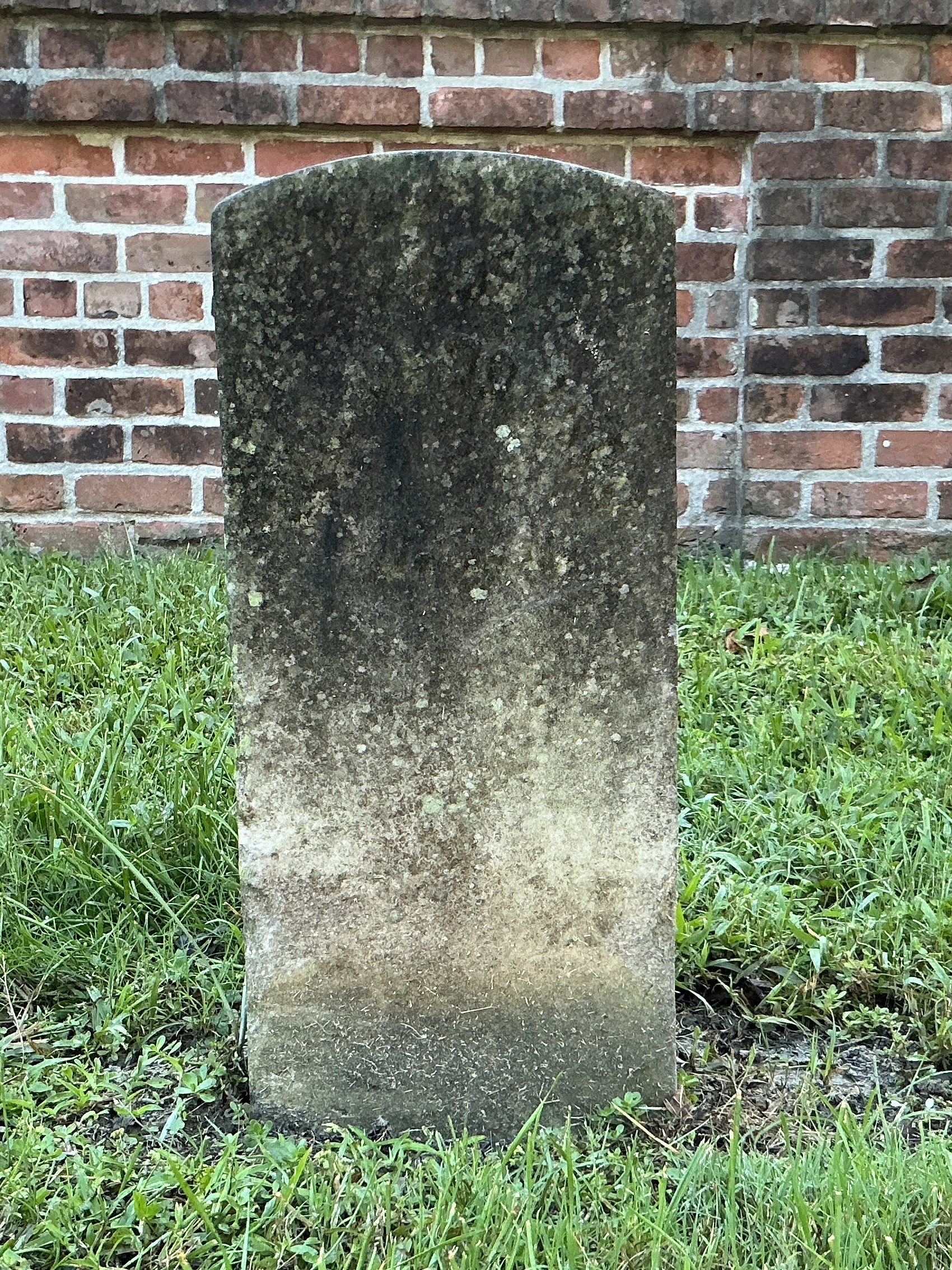 Front of historic upright marble headstone with recessed shield with recessed lettering face.