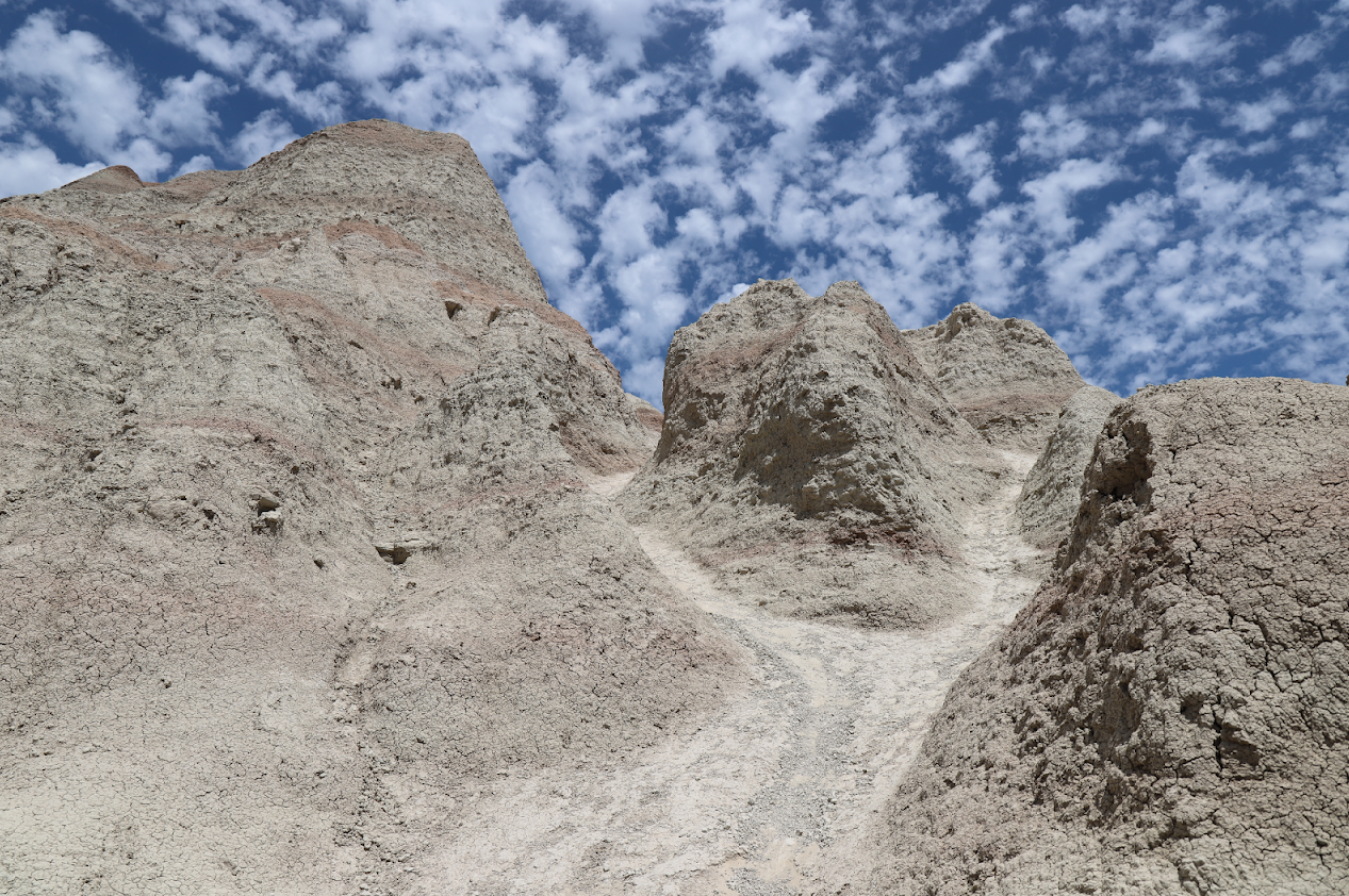 a worn trail forks in two directions headed up a steep butte with a cloudy blue sky overhead.