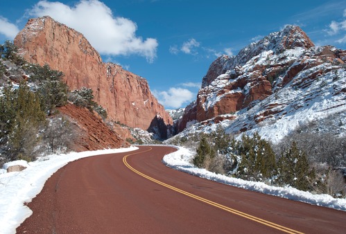 Snow is covering canyon walls as a road passes through the scene