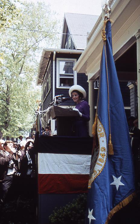 Rose Kennedy in purple suit and white hat speaks at podium