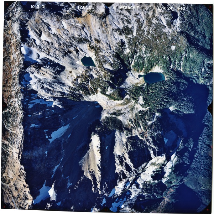 Color aerial photograph of glaciated mountain peak with forested valleys below.