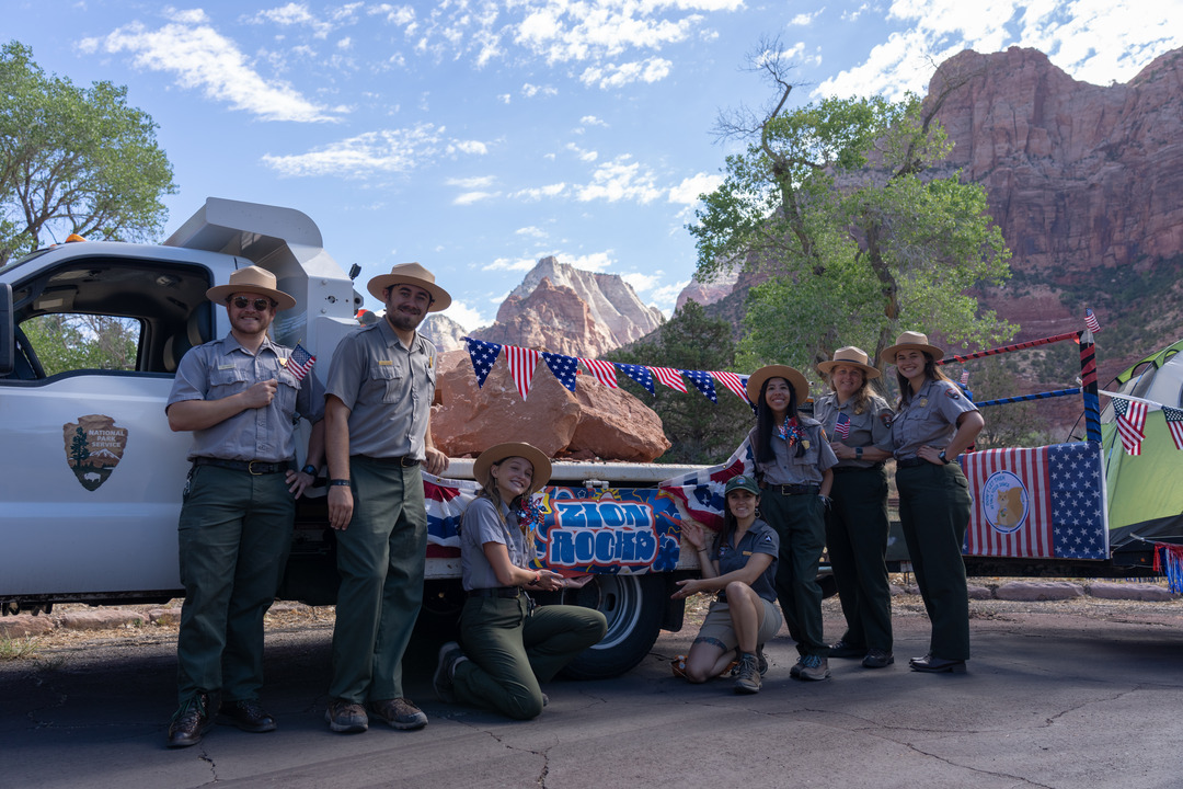 Six park rangers and a scientist in the park pose next to NPS truck decorated for the 4th of July.