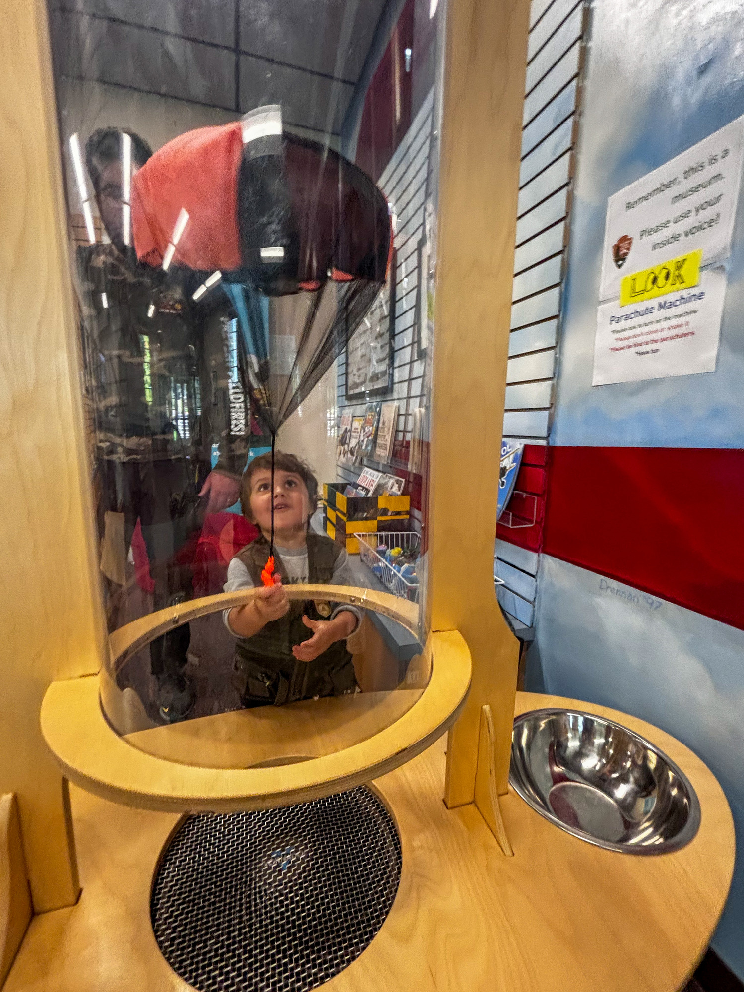 A small child looks into a clear tube, with a parachute inside. 