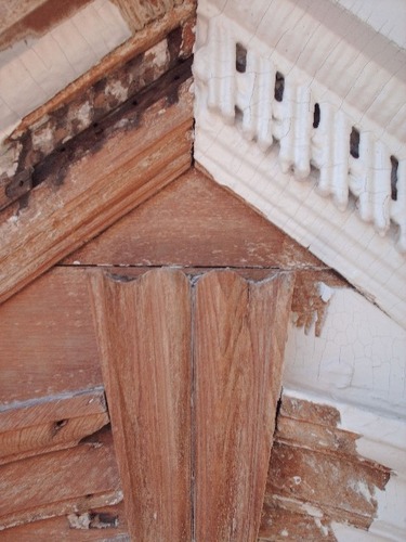 On the right, the original, degraded condition of the dormers and detailing may be seen. Dentils are caked with paing and moldings are deteriorating. On the left, paint has been stripped, dentils removed, and surfaces are prepared for restoration.