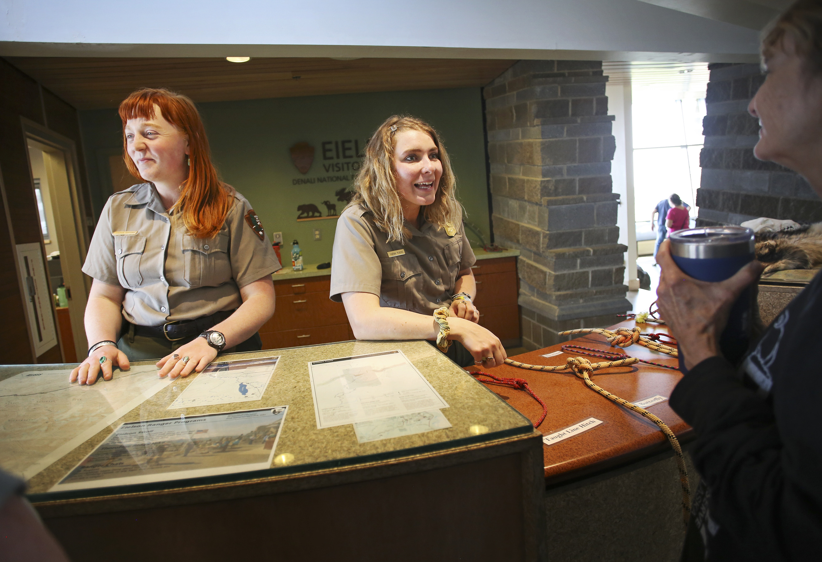 two park rangers speaking to a woman at a visitor center desk