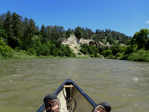 The bow of a canoe, with the paddler's feet propped up, floats down the Niobrara NSR.