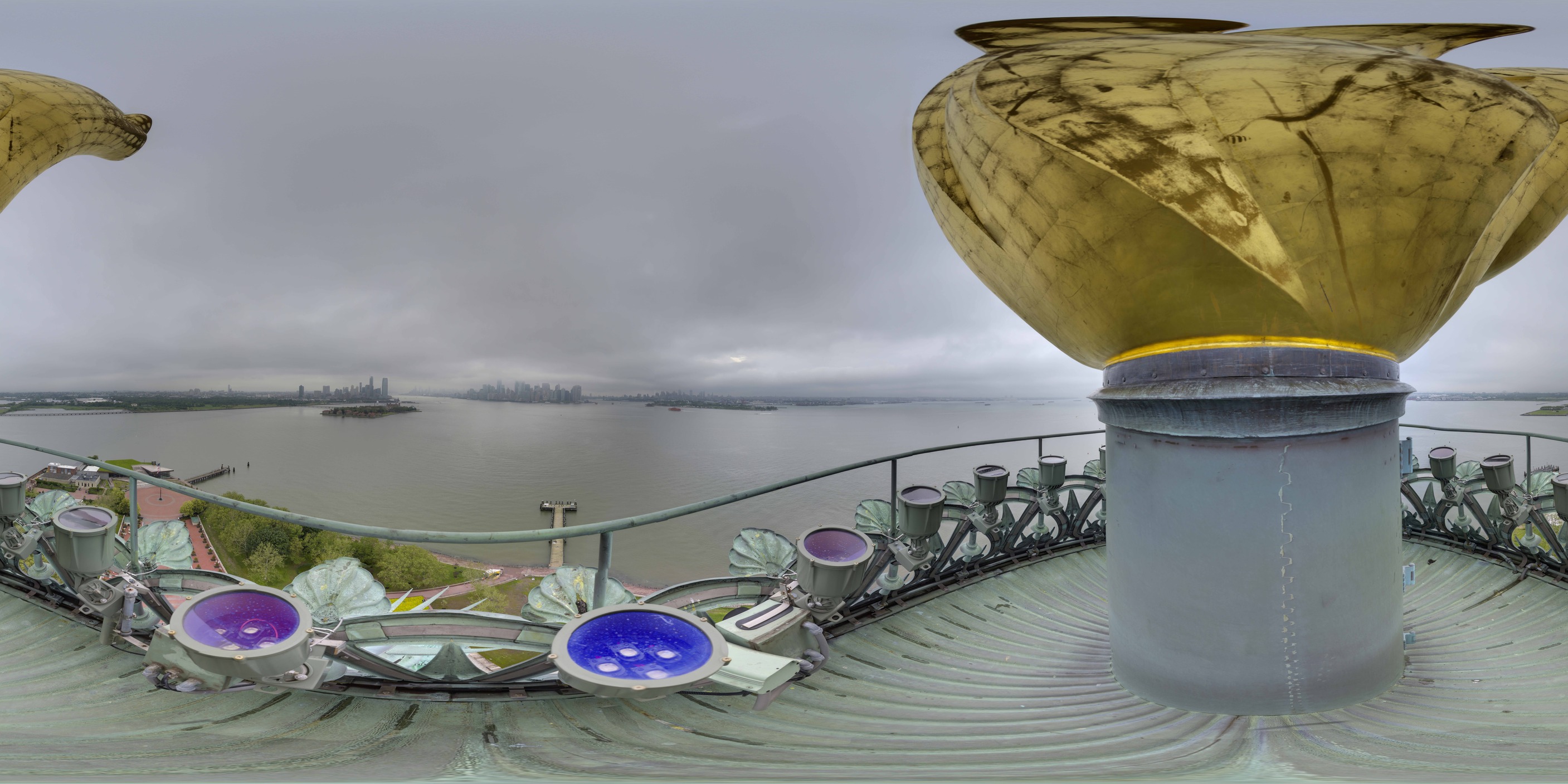 Panoramic image of view from torch balcony looking towards New York City with cloudy skies and torch flame sculpture