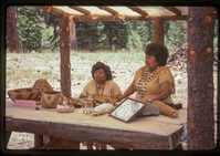 Two women stand in front of a display of Atsugewi crafts.