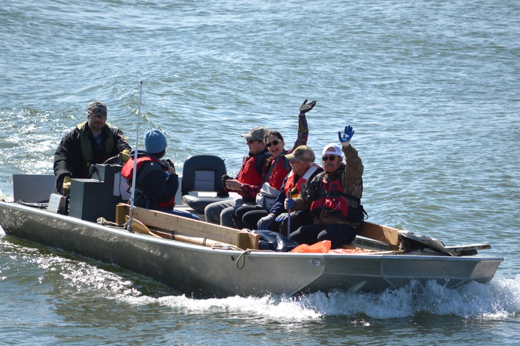 A group of people ride in a motorized boat. Two people are waving. 