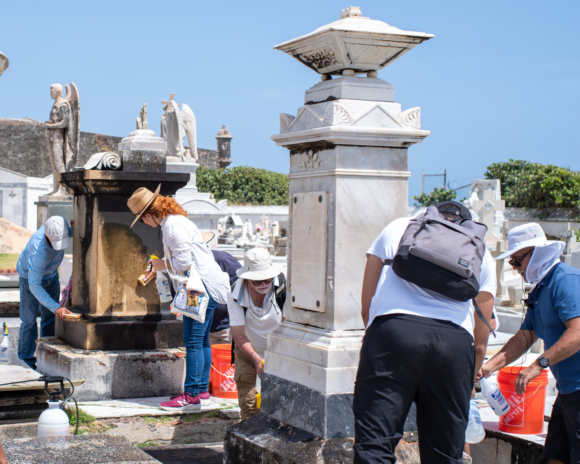 Group of people cleaning two large grave monuments with spray bottles and hand brushes