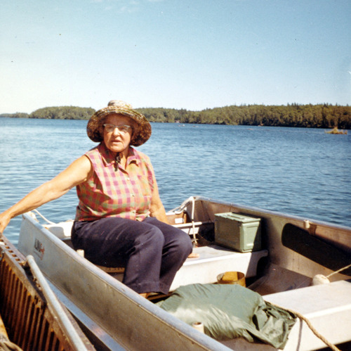 woman sitting in rowboat, wearing straw hat, holding onto dock