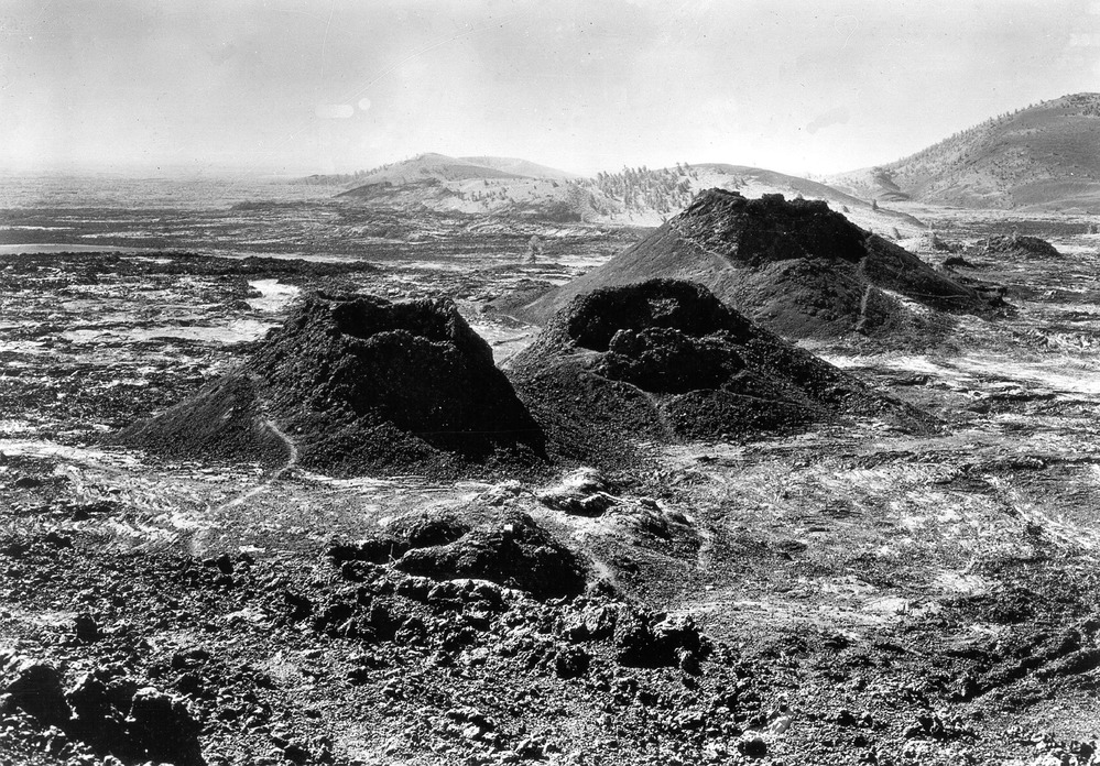 black and white photo of three spatter cones with a few trails winding around them