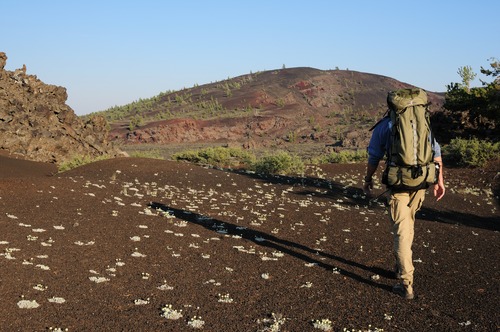 a person with a backpack hiking a cross a cinder flat toward a cinder cone