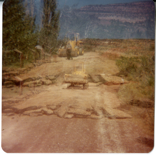 Men operating construction vehicles to clear rocks from road.