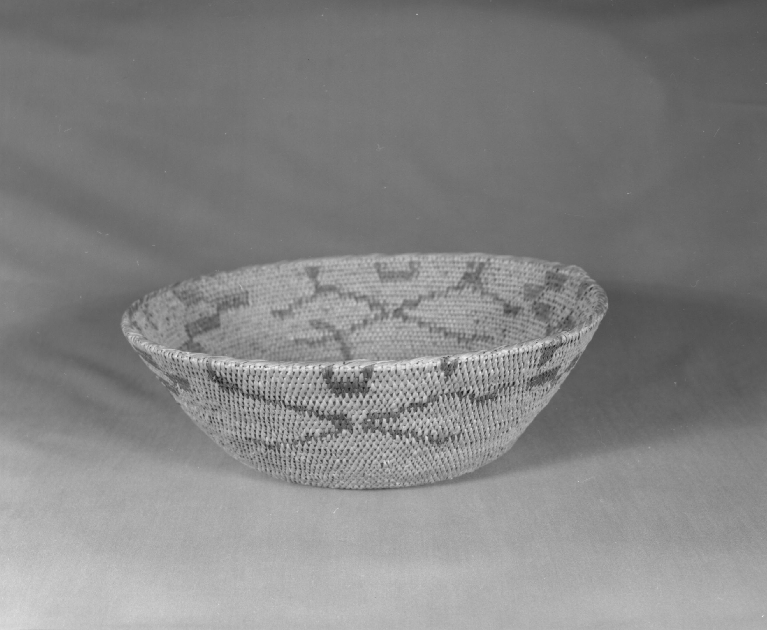 Private Collection. Object: Miwok basket. Dimensions: 12 x 3-3/4". Materials: Redbud, bracken fern, & bull pine. Technology: Single rod, fag ends trimmed on work face, moving ends trimmed on interior. Leftward coil direction. Rim overstitched three times through top rod with two back stitches at coil ending. Overstitched large clockspring start. Triangular design unit group in redbud, linear design units in bracken fern root. Collection History: Made by Matilda, 1920s. Photographed by Michael Dixon. Catalogued by Craig Bates and Barbara Beroza. Yosemite Collections, National Park Service.