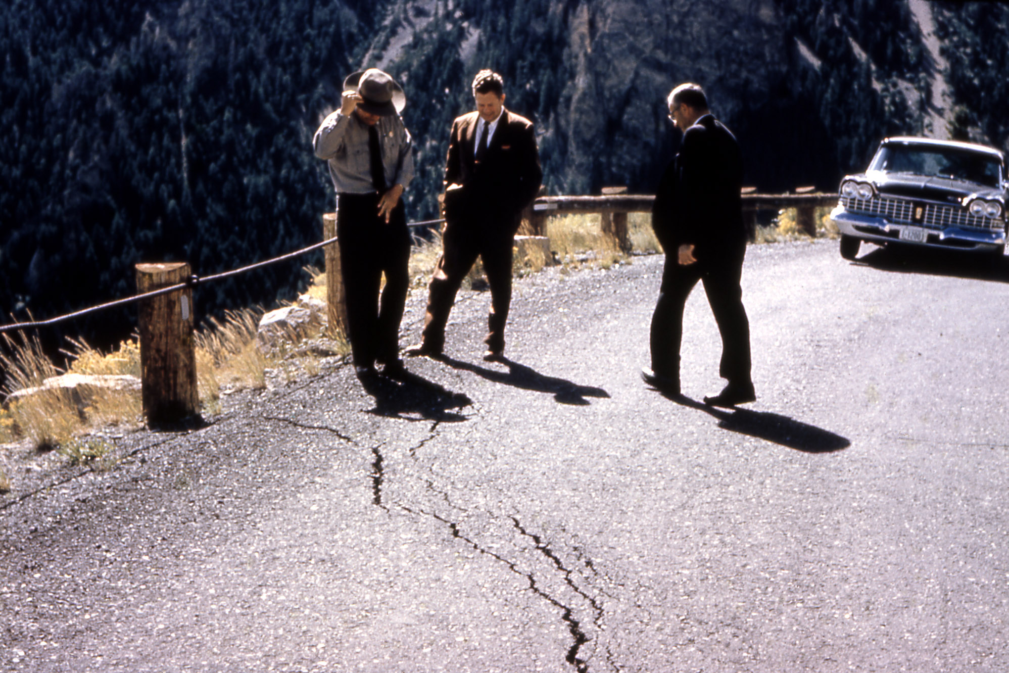 Three men looking down at a big crack in the asphalt road