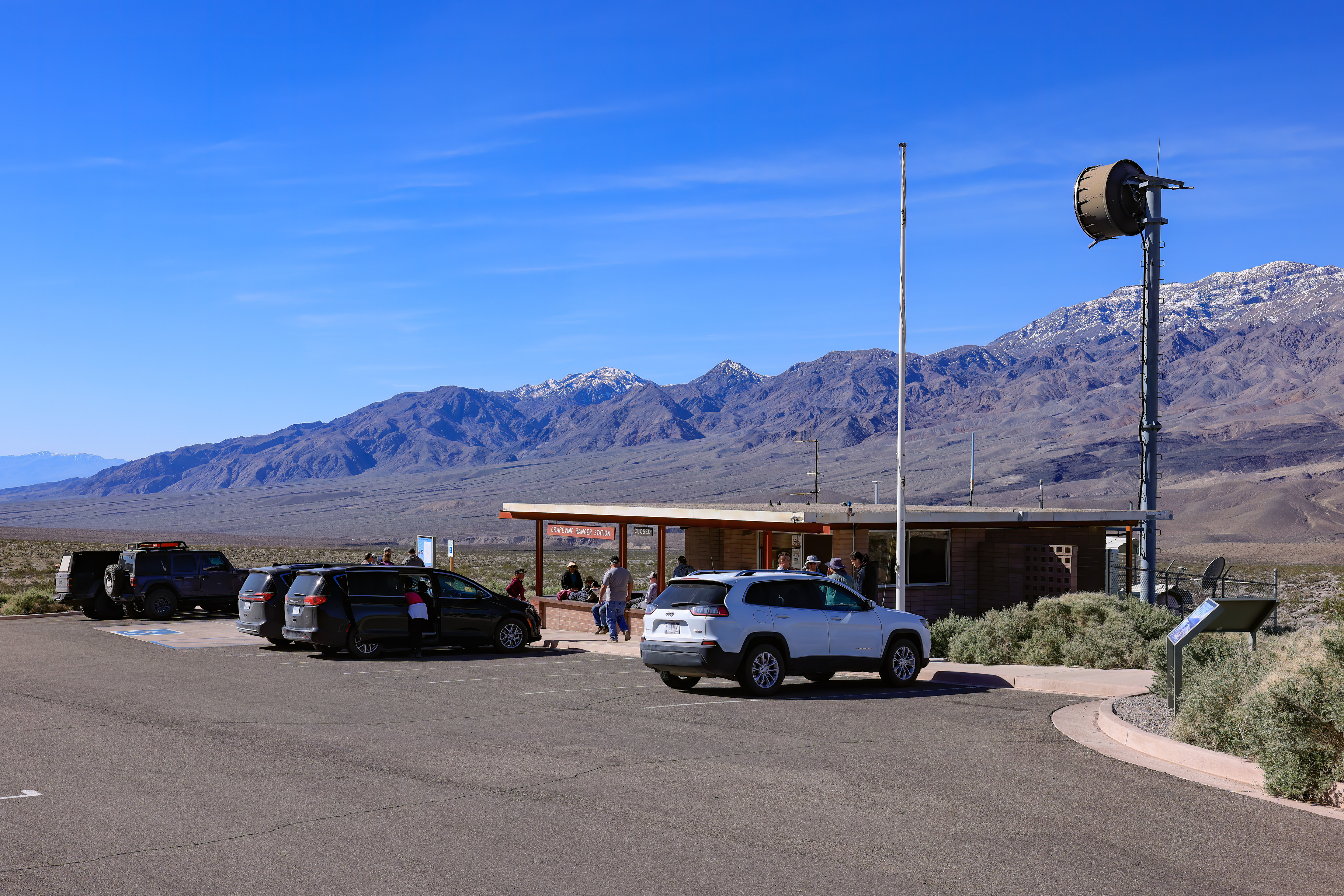 Grapevine Ranger Station parking and exterior. A small, asphalt parking lot with one accessible parking spot. A single, story ranger station with a flag pole in front of the parking area.