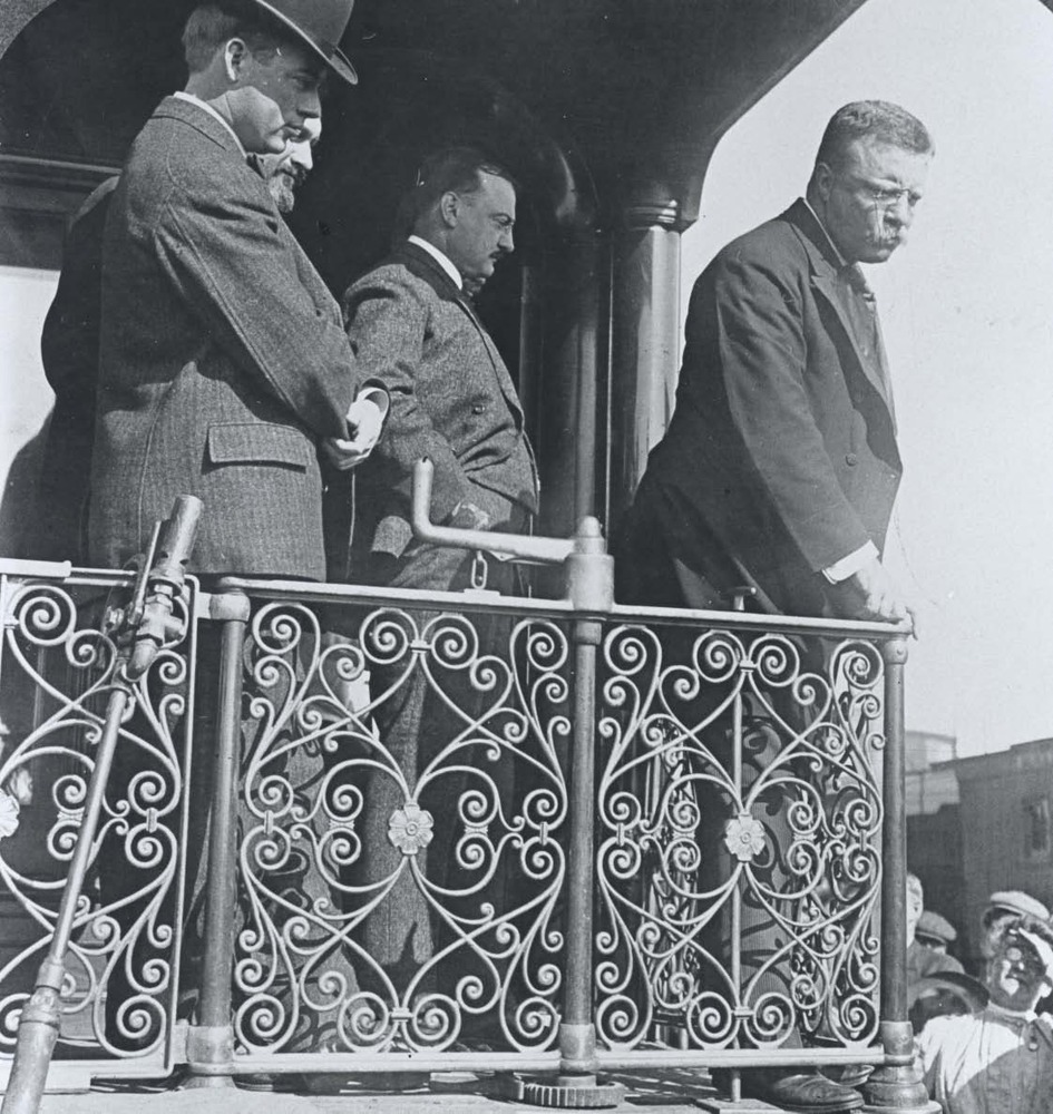 Theodore Roosevelt leans to greet people from the back of his Presidential train