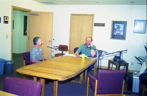 Color Photos of administration personnel. Two men with recording equipment in conference room.