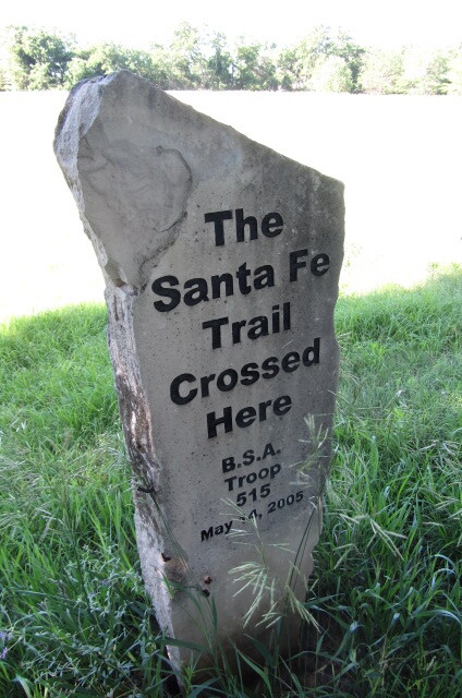 A stone marker with the words "The Santa Fe Trail Crossed Here B.S.A. Troop 615 May 2005" on it, standing in the grass.