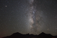 Stars shine as the Milky Way backlights the silhouette of a mountain range.