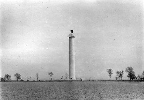 Memorial column in center dwarfing the few trees around. Water in foreground.