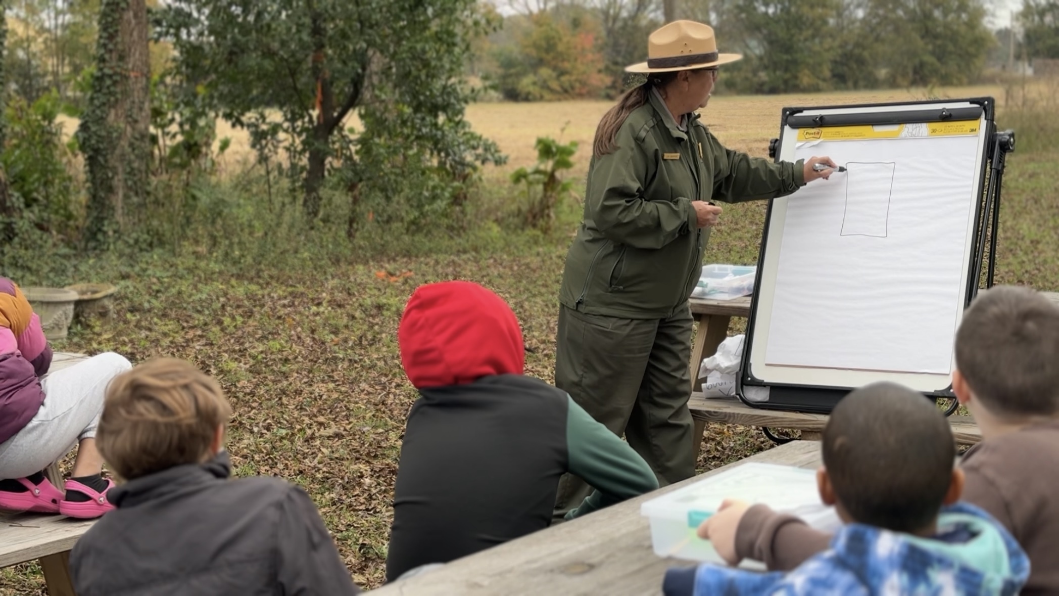 Park ranger drawing a square on paper outside. Students in foreground. 