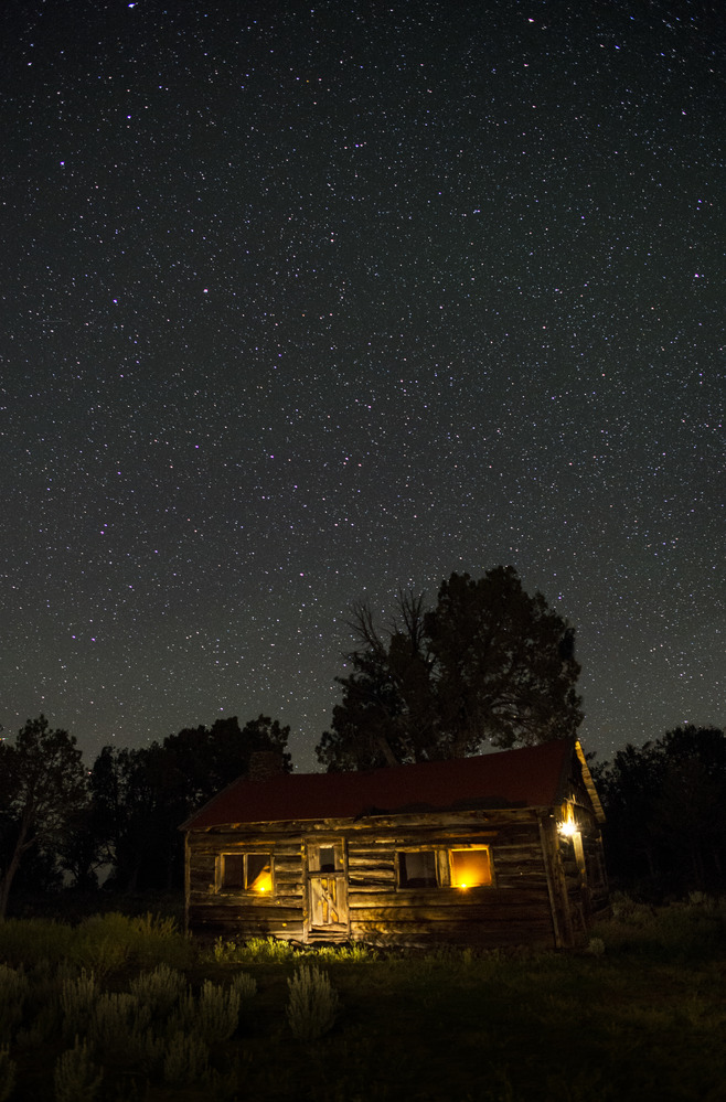 An old ranch house with lights in the windows and a starry night sky.