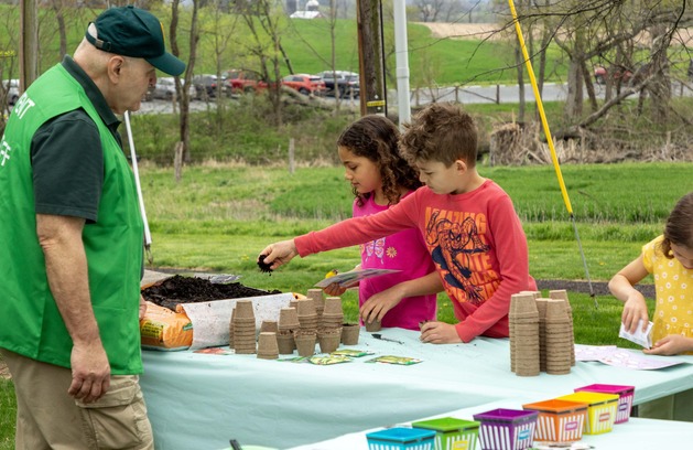Two children stand at a table with cups and soil. 