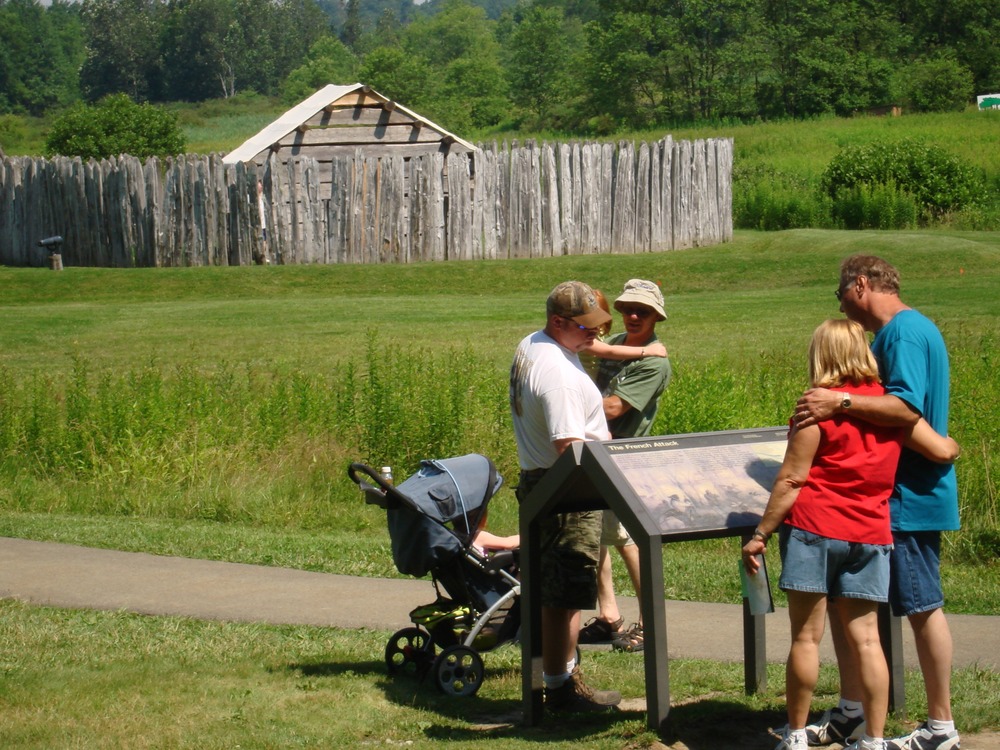 Visitors reading outdoor exhibits with Fort Necessity in background