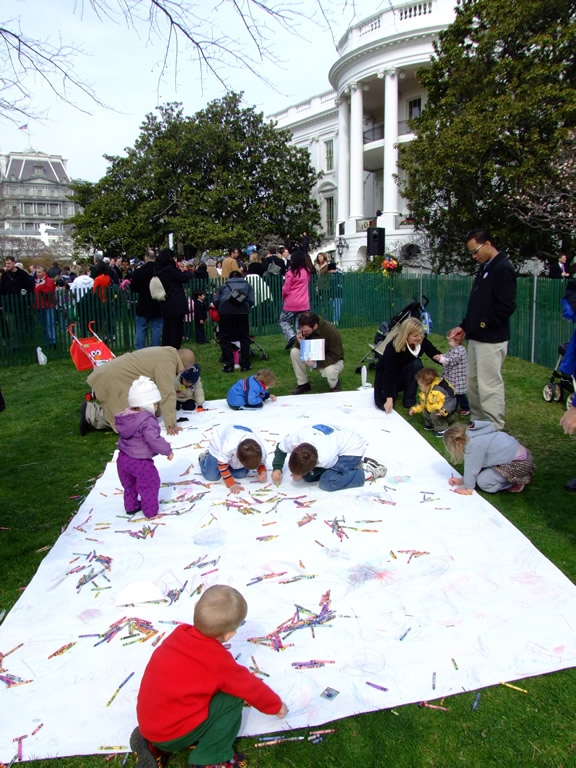 Several children paint a large white canvas. 