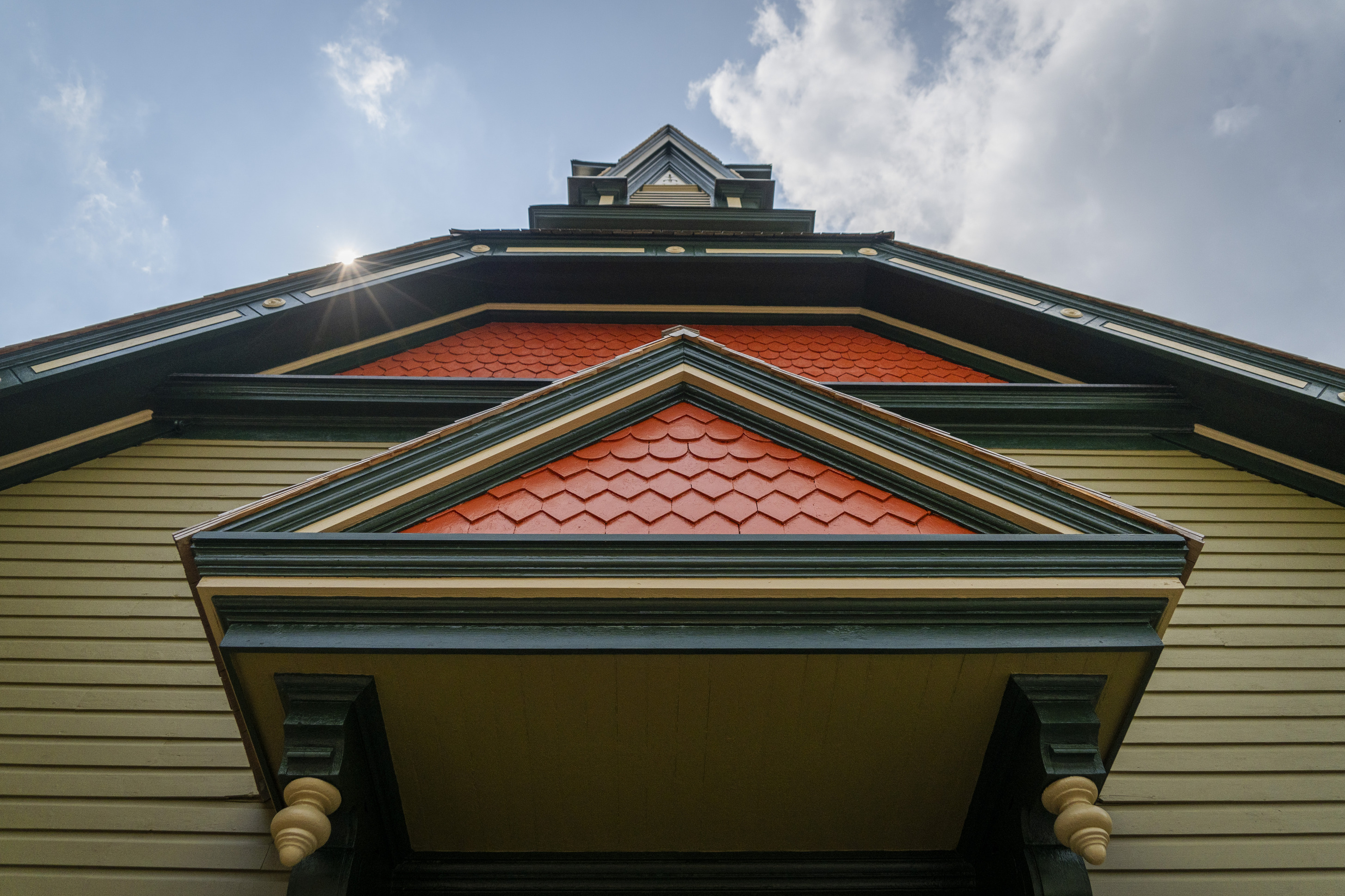A low angle looking up toward the steeple of a green, orange, and yellow church building.