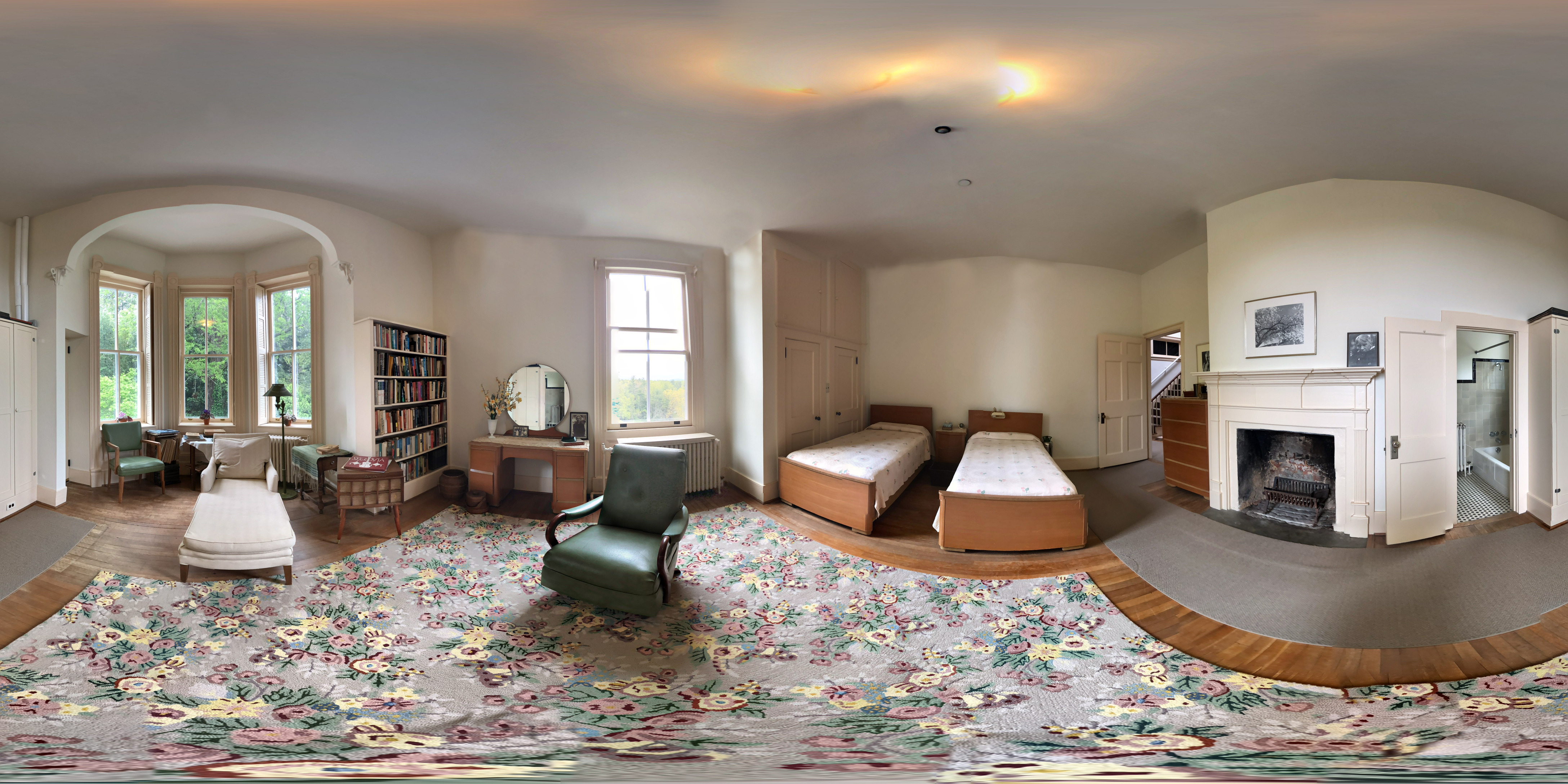 360 image of a bedroom with 2 twin beds, a large bay window, dressers, bookshelf and 2 comfortable lounge chairs in the center.