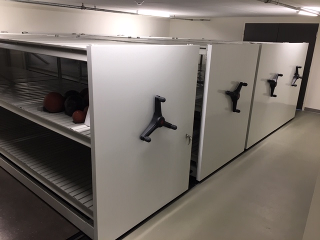 Several cannonballs sit on compact shelving in a white room.