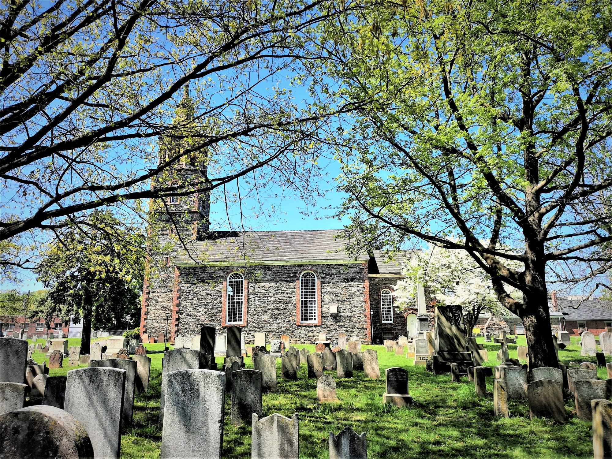 Masonry church, with steeple, and cemetery, with many gravestones. Trees and grass are also visible. 