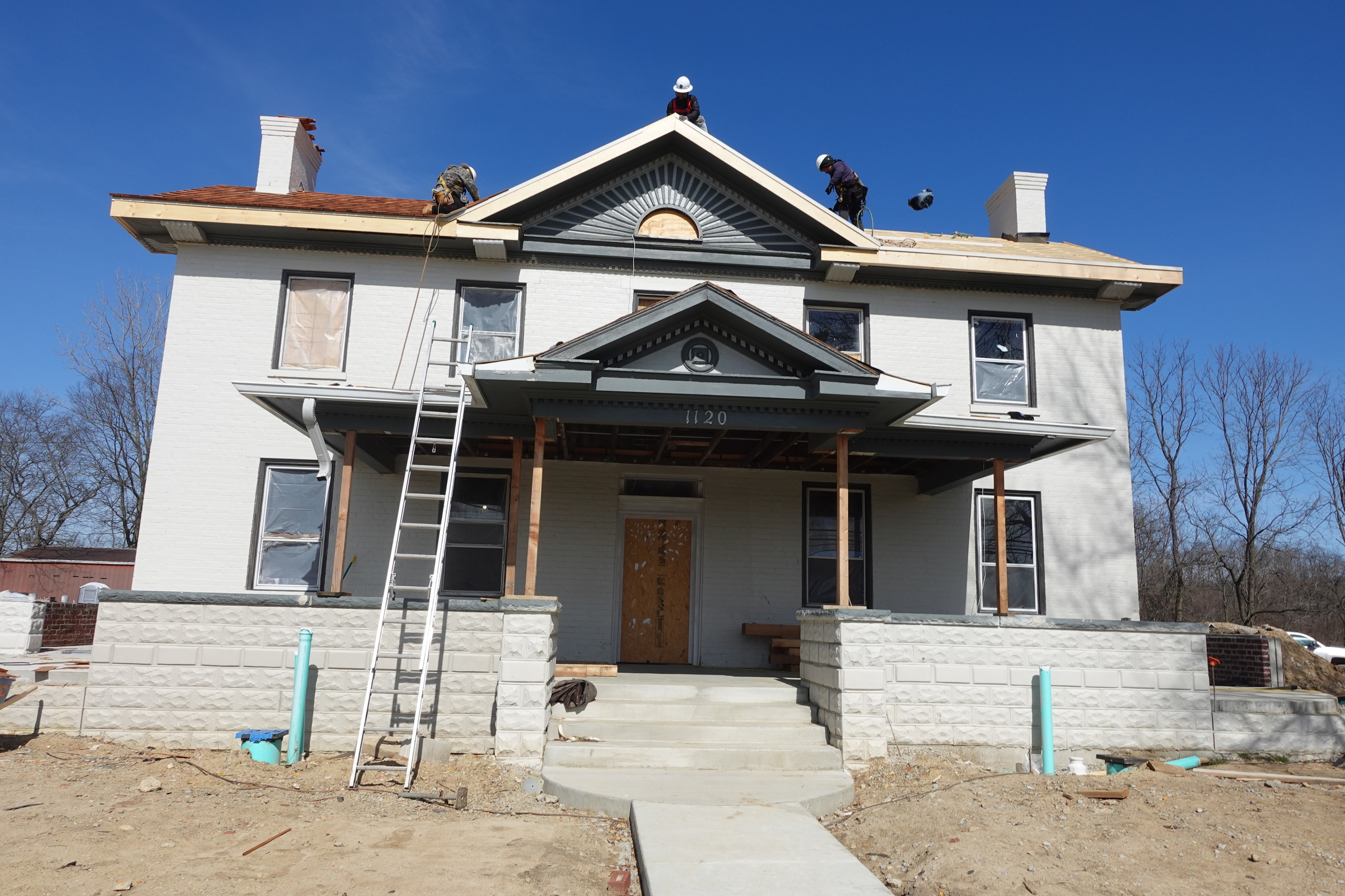 Two story grey brick home under construction with three male construction workers on the roof.