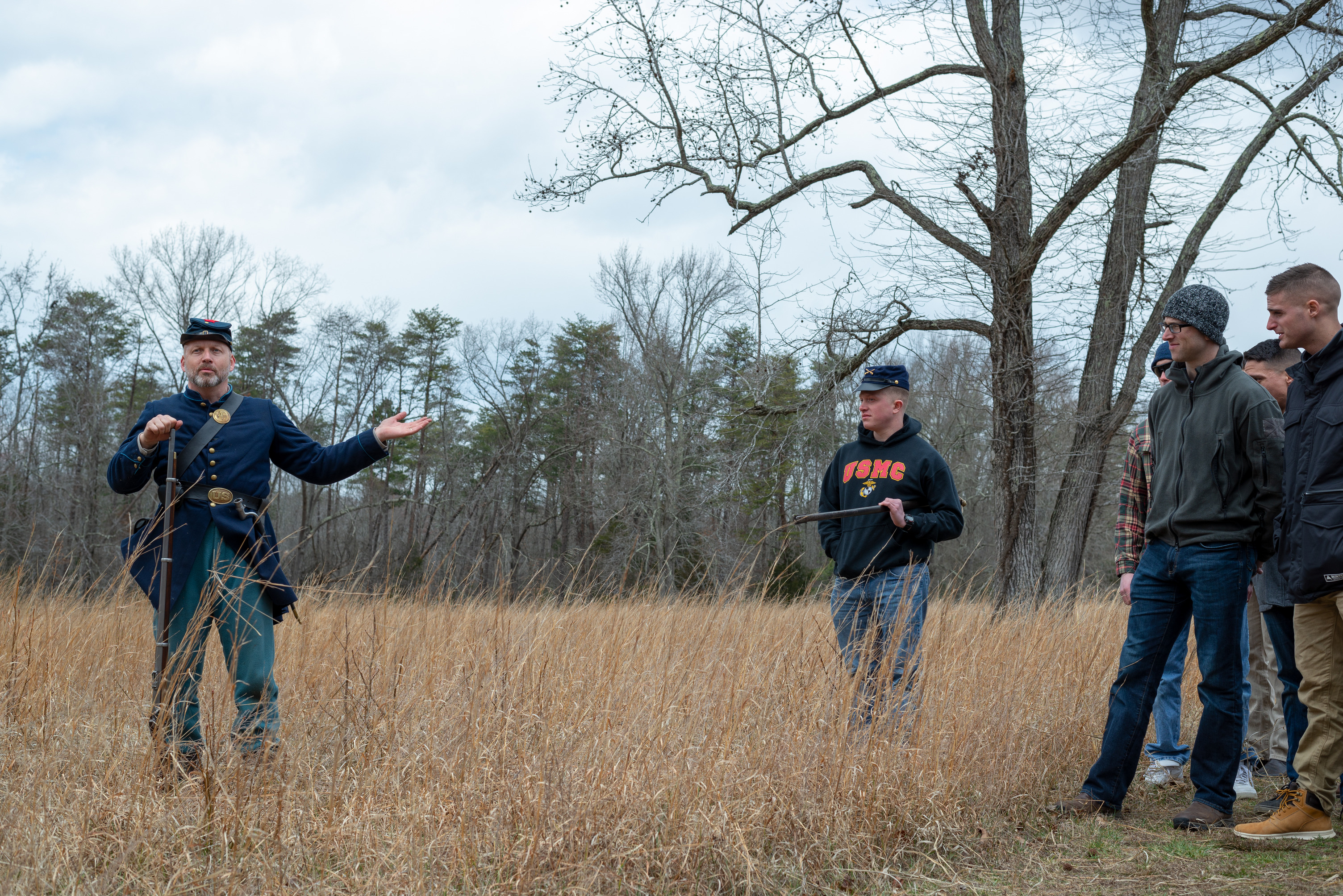 A man in a Civil War Union uniform stands in a field with a group of five men facing him.