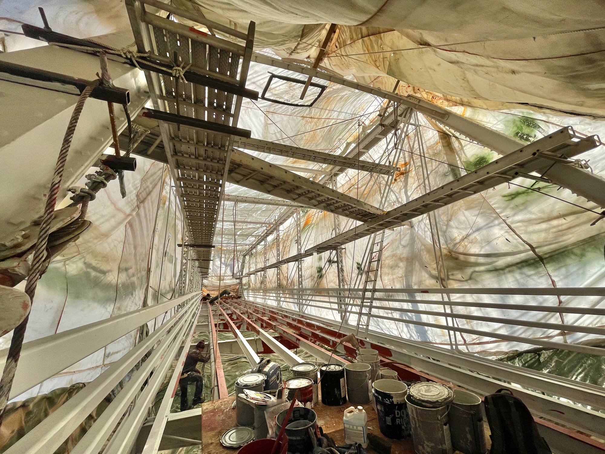 Suspended walkways run down each side of the bridge, with two spanning the width. Most of the trusses have been painted, but some red primer still shows.