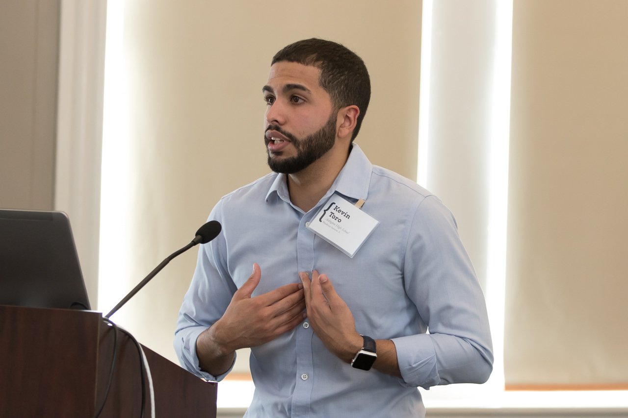 A man speaking into a microphone and holding hands to his chest. 