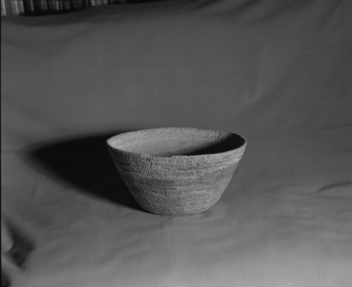 Private Collection. Object: Miwok basket. Dimensions: 10 1/2 x 5 1/2". Materials: Split bull pine and redbud. Technology: Single rod, interlocking stitch, fag ends trimmed on workface, moving ends trimmed on interior and some bound under. Original rim missing. Five vertical design units of stacked inverted tree like forms. Encrustation, probably from acorn. Collection History: Purchased from Maggie Longfellow's mother, also known as Mrs. Longfellow Poncho. Photographed by Michael Dixon. Catalogued by Craig Bates and Barbara Beroza. Yosemite Collections, National Park Service.