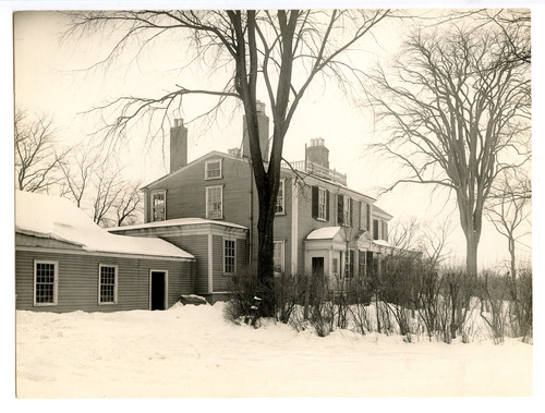 Black and white photograph of mansion with several additions in snow.