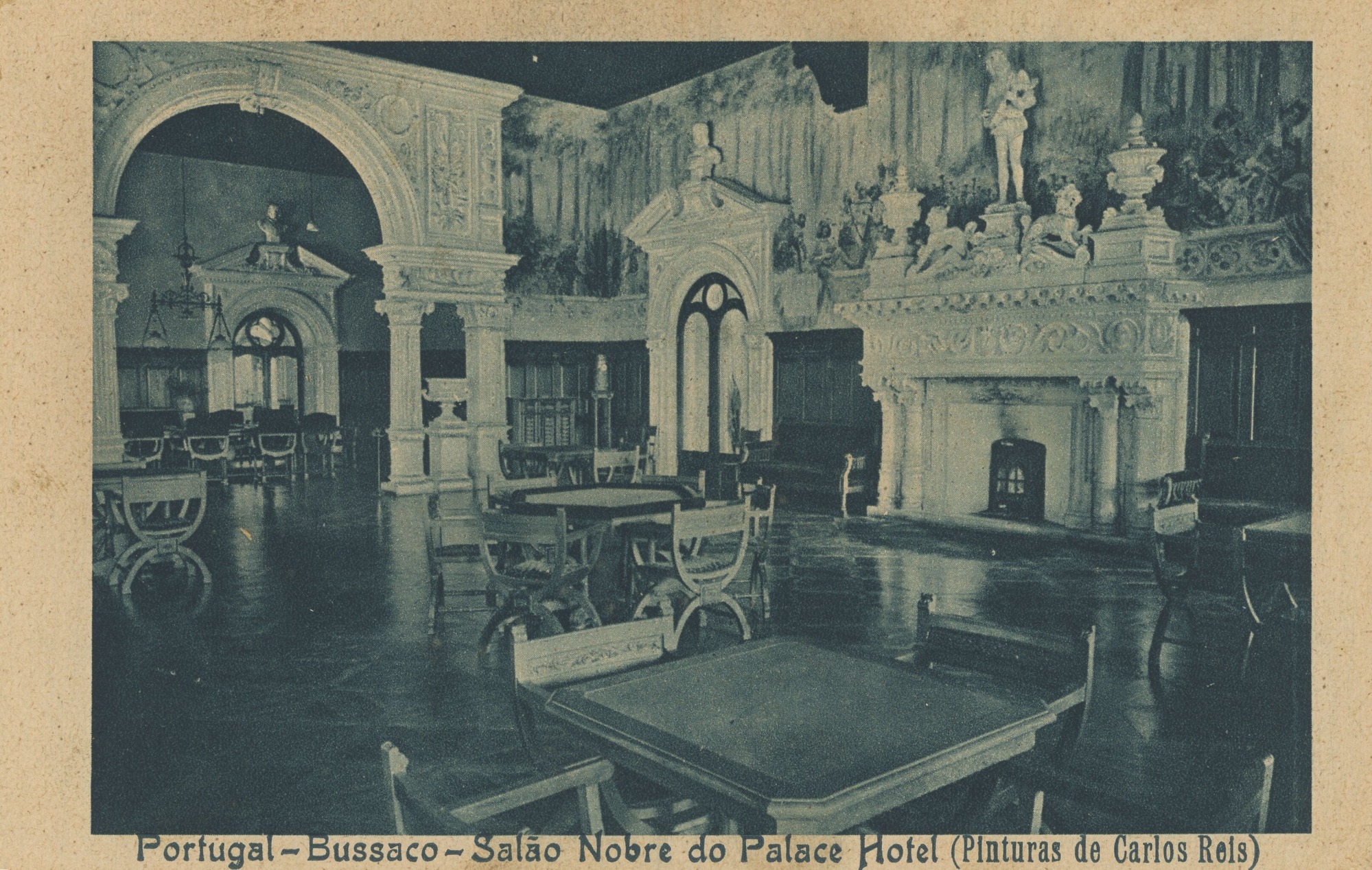 Post card with a printed blue-toned photograph of the interior of a hotel dining room. The interior is vacant and lavishly decorated. Two tall doors are visible with bust sculptures built into the top. Scattered along the marble floor are many tables and chairs. On the right side, a large fireplace at the wall is sculpted with patterns, and two horses, two vases, and a person playing a string instrument is built into the mantle. A mural of a forest scene is painted on the top portion of the righthand wall. Towards the left side, a large decorated archway shows another section of the dining room with tables, chairs, and a low-hanging chandelier. At the bottom, printed writing reads, “Portugal-Bussaco-Salão Nobre do Palace Hotel (Pinturas de Carlos Reis).”