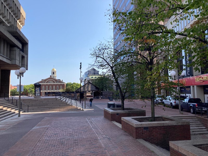 Open plaza with brick pavement and steps on one side, and buildings on either side of plaza, and at the end of the plaza, in the distance, a historic brick three-story church and modern building adjacent