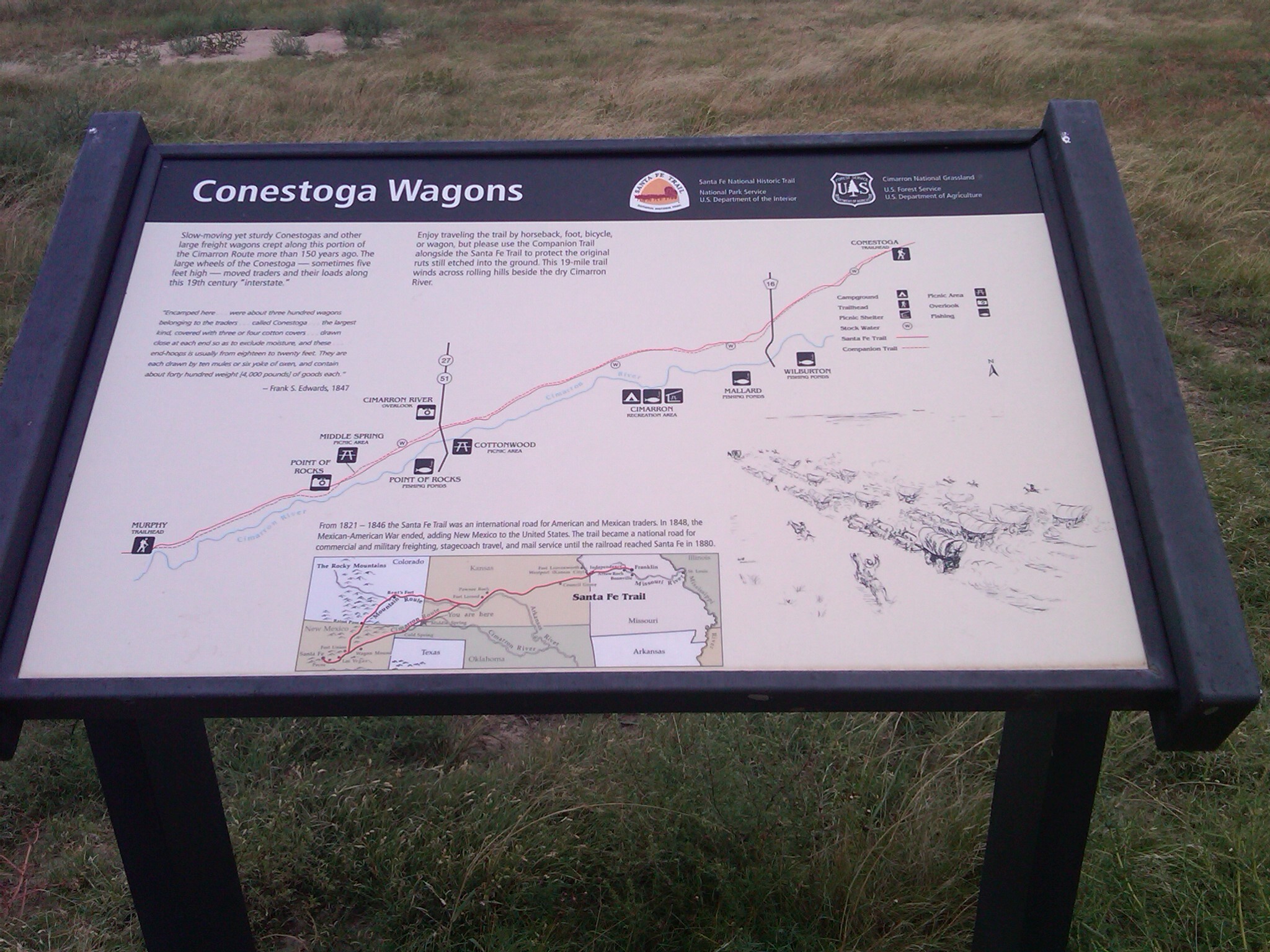 A wayside titled "Conestoga Wagons" with some text and illustration on it in a grassy field.